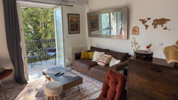 A living room with a sofa, coffee table, and a view of a balcony with outdoor furniture.