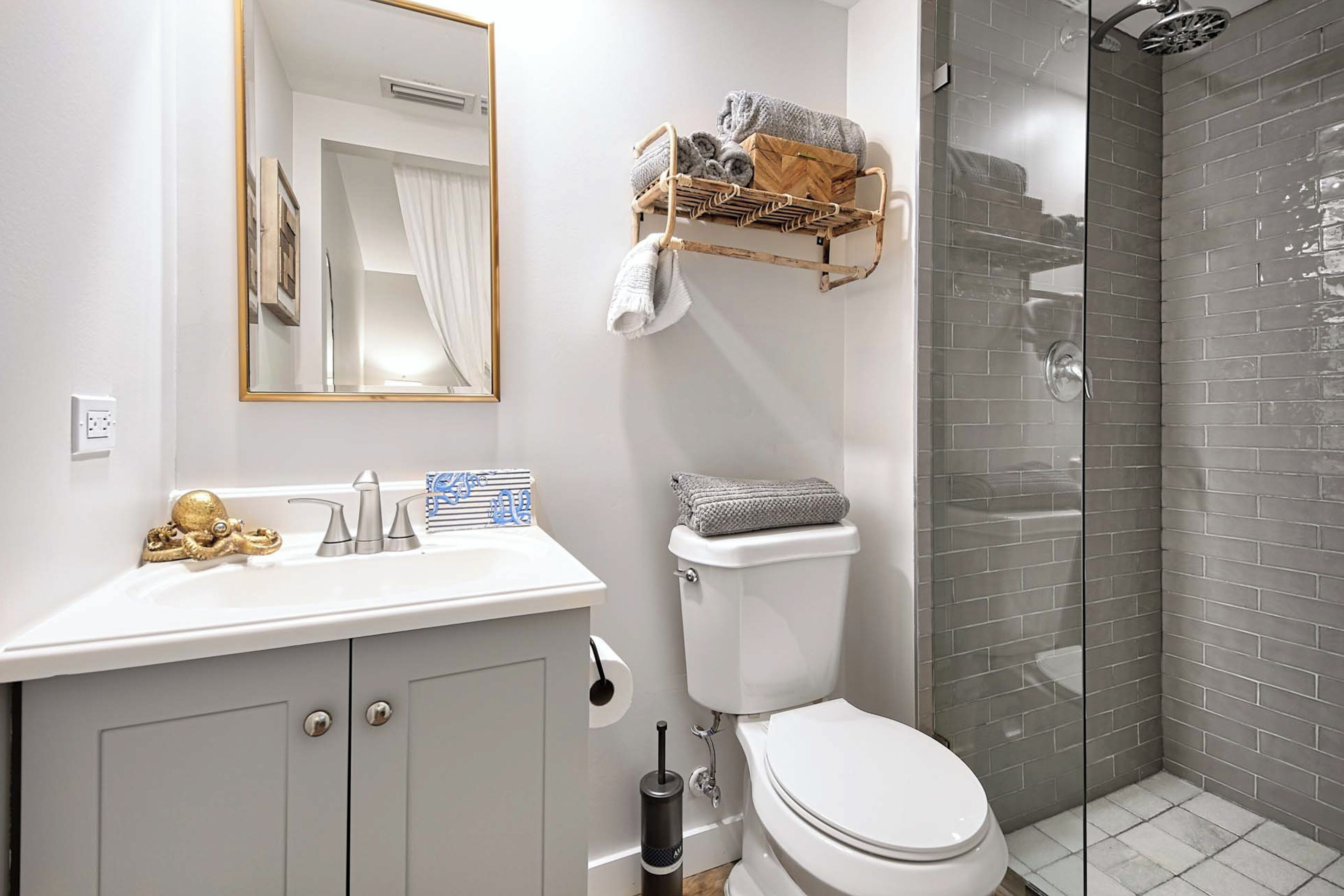 Een badkamer met een wit toilet, een wastafel met een gouden decoratie, een handdoekrek met handdoeken en een douchecabine van glas.