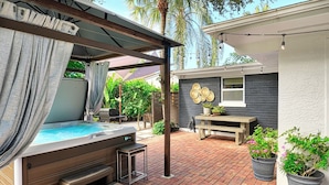 A patio area with a hot tub, wooden steps, a table, and potted plants. - Near Old Naples! Coastal Escape w/ Tropical Patio (Naples)