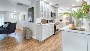 A modern kitchen with white cabinets, a microwave, and a stove. There is a black chair and two woven baskets on the floor. - Near Old Naples! Coastal Escape w/ Tropical Patio (Naples)