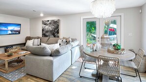 A modern living room with a grey sofa, a round dining table with wicker chairs, a chandelier, and artwork on the walls. - Near Old Naples! Coastal Escape w/ Tropical Patio (Naples)