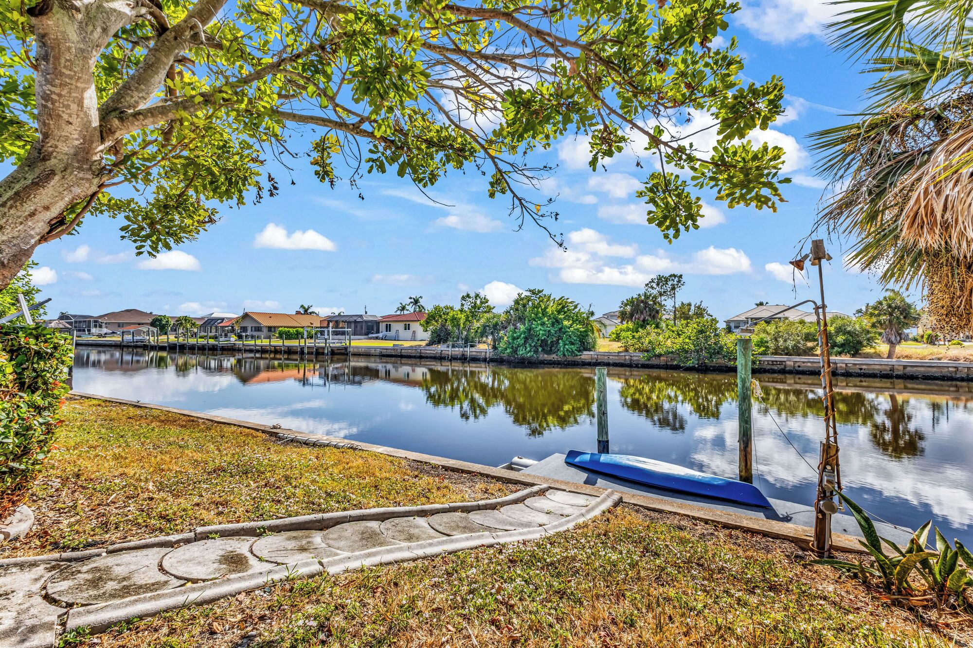 A calm water body with a dock, surrounded by greenery and houses in the background.