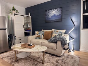 Ein Wohnzimmer mit einer Couch, einem Couchtisch, einem Bücherregal und einem an der Wand befestigten Fernseher.