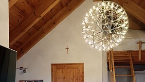 A cozy room with a wooden ceiling, a wooden door, a TV, a chair, a ladder, and a hanging light fixture. - Apartment "Blütenlicht" with Mountain View, Shared Terrace and Wi-Fi (Hameln)