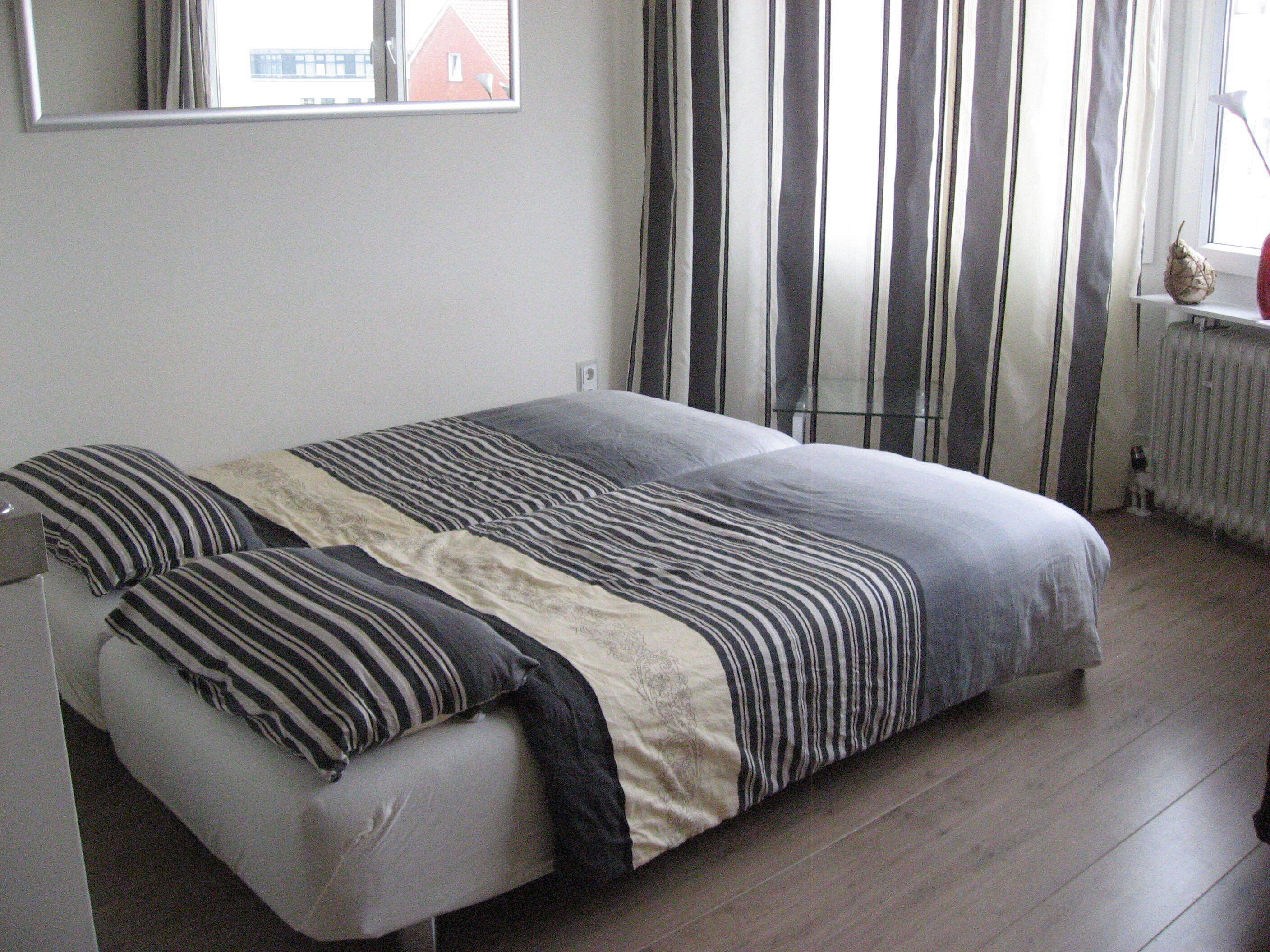 Una camera da letto con un letto, una finestra con tende, un termosifone e una piccola pianta su uno scaffale.