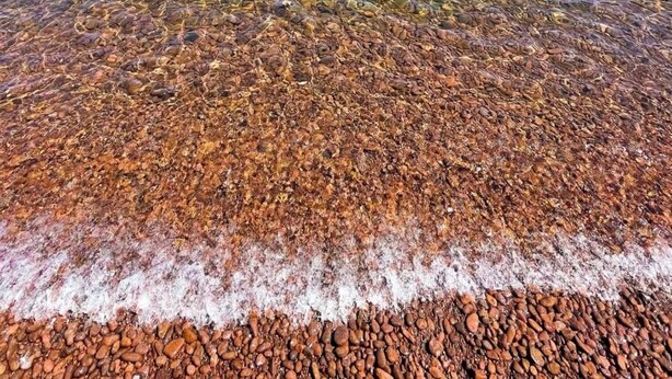 Vista despejada de una playa de guijarros, aguas tranquilas y acantilados rocosos.