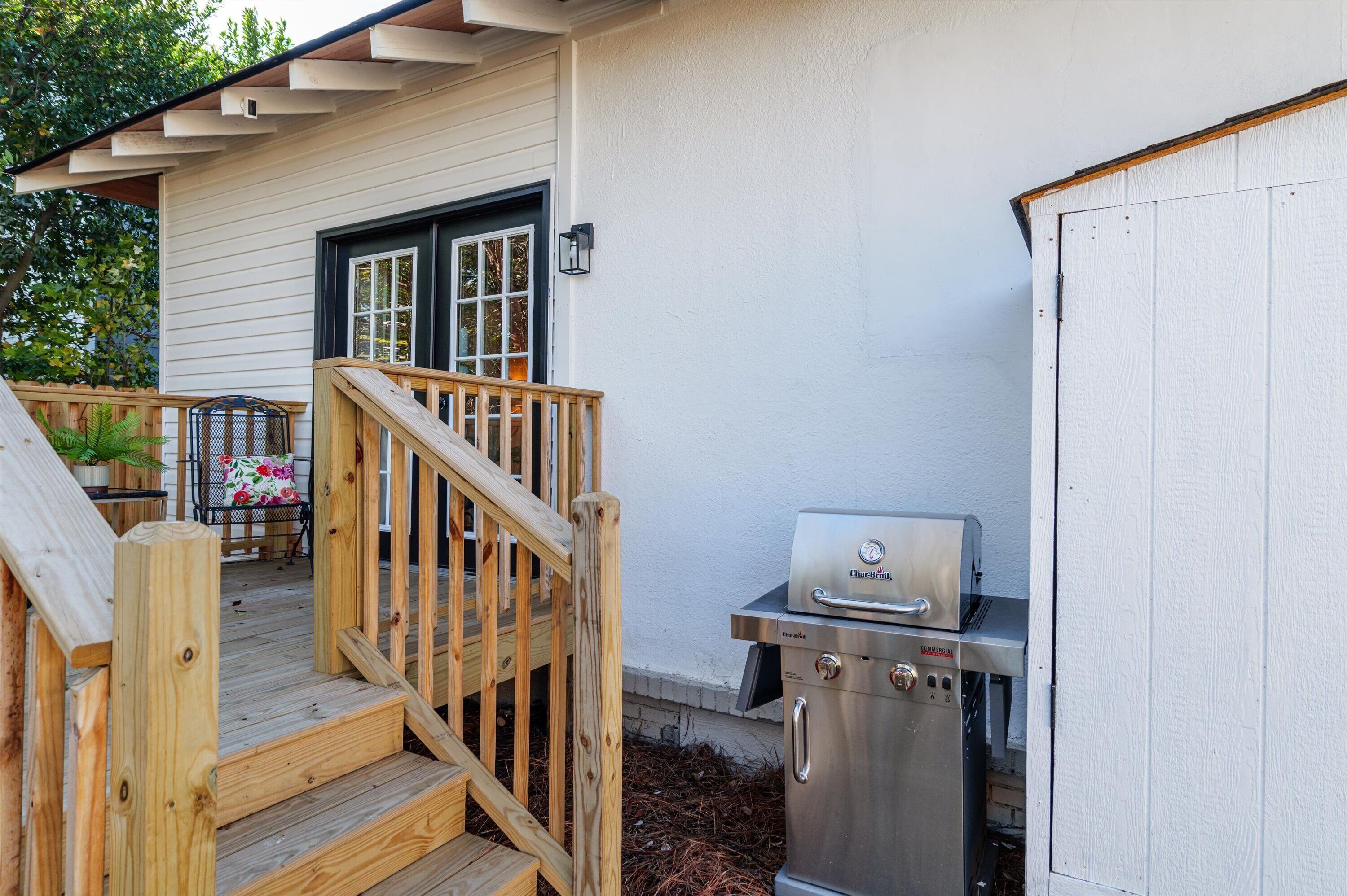 A wooden deck with a grill and a chair with a floral cushion.