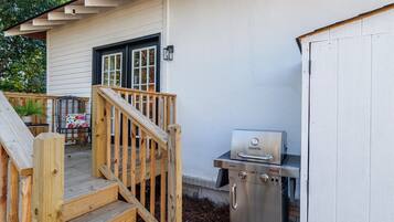 A wooden deck with a grill and a chair with a floral cushion.