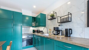 Een moderne keuken met blauwgroene kastjes, een ingebouwde oven en een koffiezetapparaat.