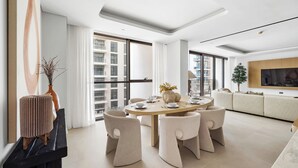 Un salon moderne avec une table à manger ronde, des chaises de couleur beige, un canapé et un téléviseur fixé au mur.