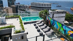 A rooftop pool area with lounge chairs and a glass barrier, overlooking a cityscape and a bridge. - Modern apartment in Rio de Janeiro + swimming pool + rooftop with panoramic views. (Rio de Janeiro)