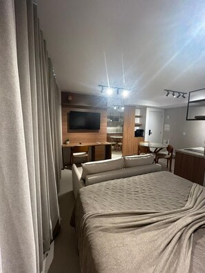 Een hotelkamer met een groot bed, een aan de muur bevestigde televisie, een bureau met stoel en een zithoek met tafel en stoelen.