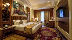 Una habitación de hotel amplia con una cama grande, un escritorio, una silla, un televisor y un mural decorativo en la pared.