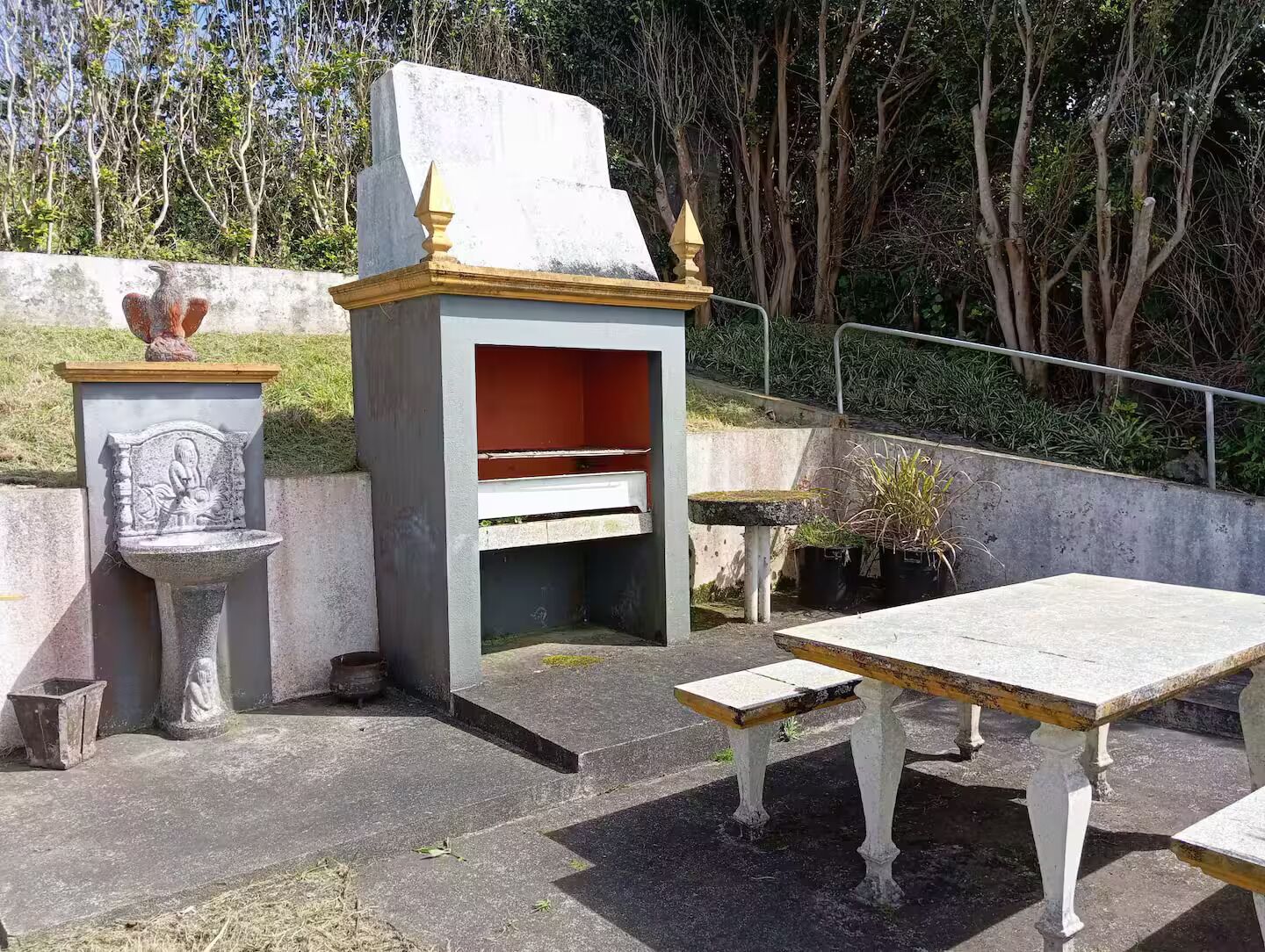 Een stenen bank met een tafel, een stenen sculptuur en een kleine tuin met planten.