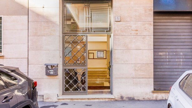 A building entrance with a metal gate, a staircase leading inside, and a garage door to the right. - Domus Appia by Rentbeat (Roma)
