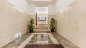 A hallway with a reflective floor, a central rug, and potted plants on either side. - Domus Appia by Rentbeat (Roma)