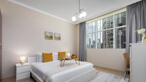 A modern bedroom with a large bed, bedside tables, a nightstand, a dresser, a chair, and a window with curtains. - Maison Privee - Modern Downtown Apartment w/ City Skyline Vws (Dubai)