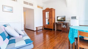 Una habitación con piso de madera, un sofá con cubierta azul y blanca, un mueble de madera, un escritorio con una computadora y una mesa con mantel azul.