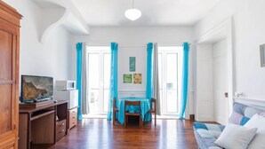 Una habitación amplia con un escritorio de madera, televisión, zona de comedor con mesa y sillas, y un sofá.