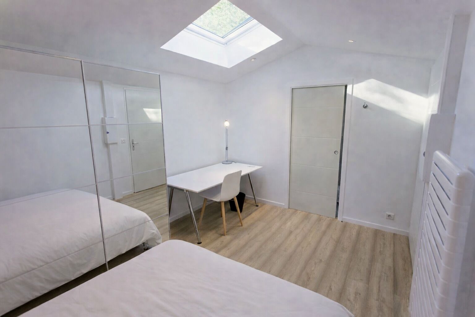 A modern bedroom with a skylight, two beds, a desk, and a radiator.