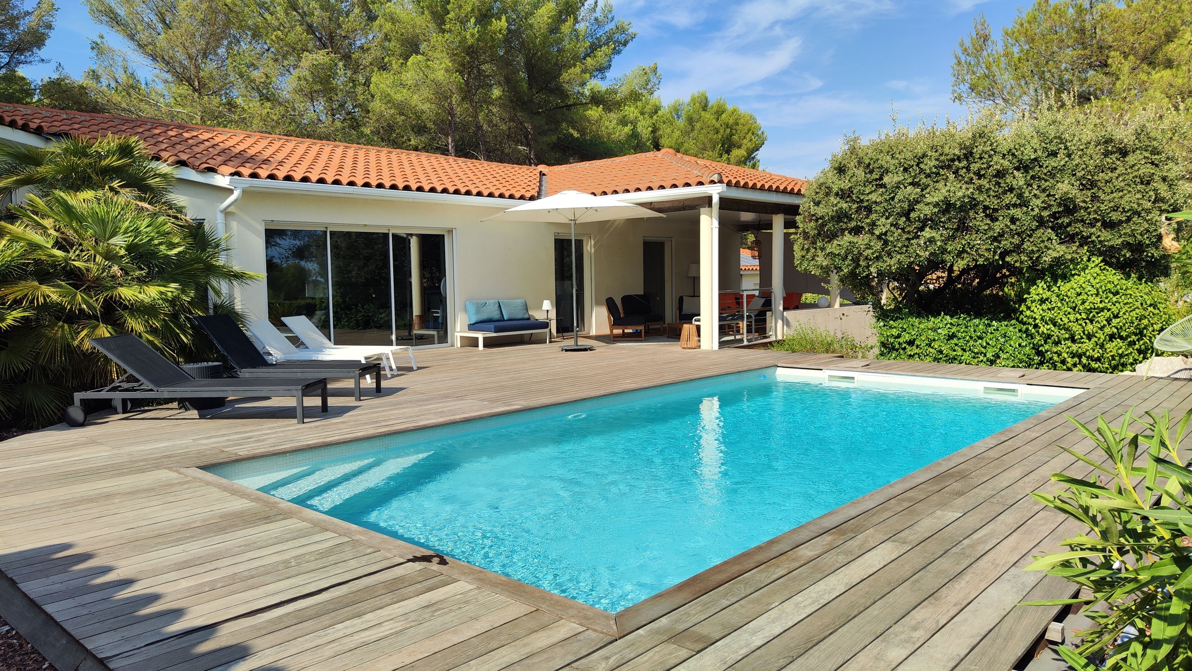 Une piscine avec une terrasse en bois, des chaises longues et un patio couvert.