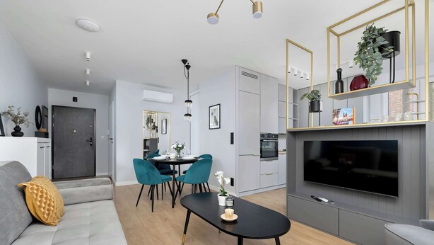 Ein modernes Wohnzimmer mit einer Couch, einem Couchtisch und einem an der Wand befestigten Fernseher. Es gibt einen Essbereich mit Stühlen und einem Tisch, sowie eine Küche mit Schränken und einem Herd.