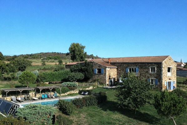 Une maison en pierre avec une piscine, entourée de verdure et sous un ciel dégagé.