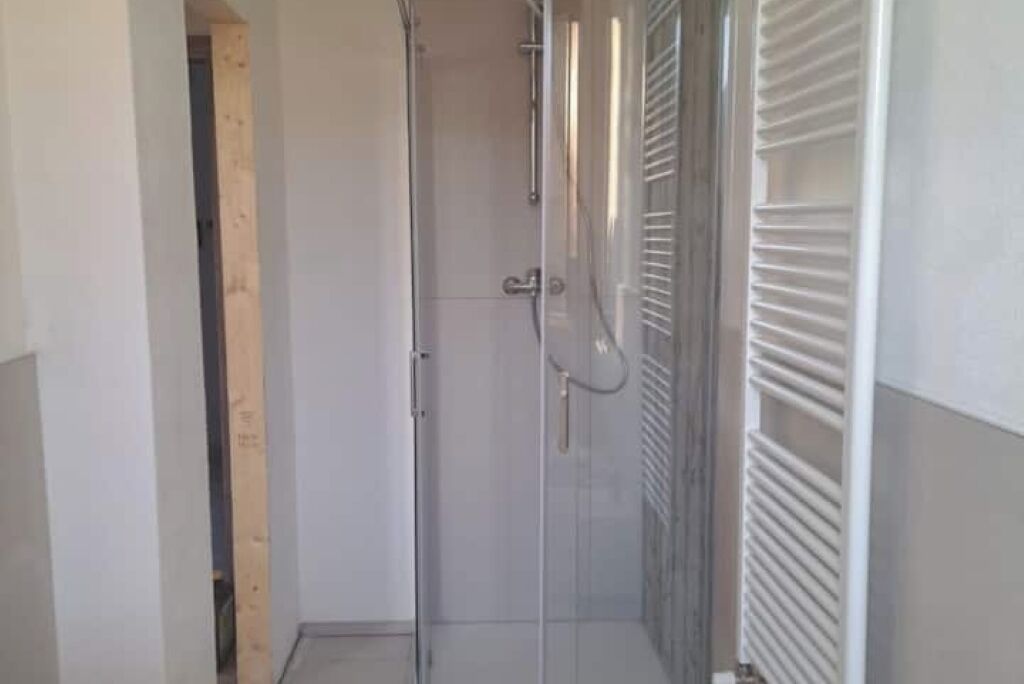 Box de chuveiro pequeno e fechado, com porta de vidro, puxador de metal e porta-toalhas branco à direita.