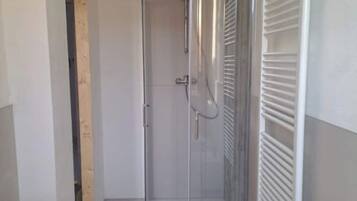 Box de chuveiro pequeno e fechado, com porta de vidro, puxador de metal e porta-toalhas branco à direita.