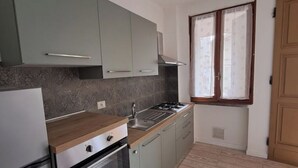 A kitchen with a stove, oven, and sink, light green cabinets, and a window with curtains. - Casa i Sodi - Relaxation with mountain views (Castiglione dei Pepoli)