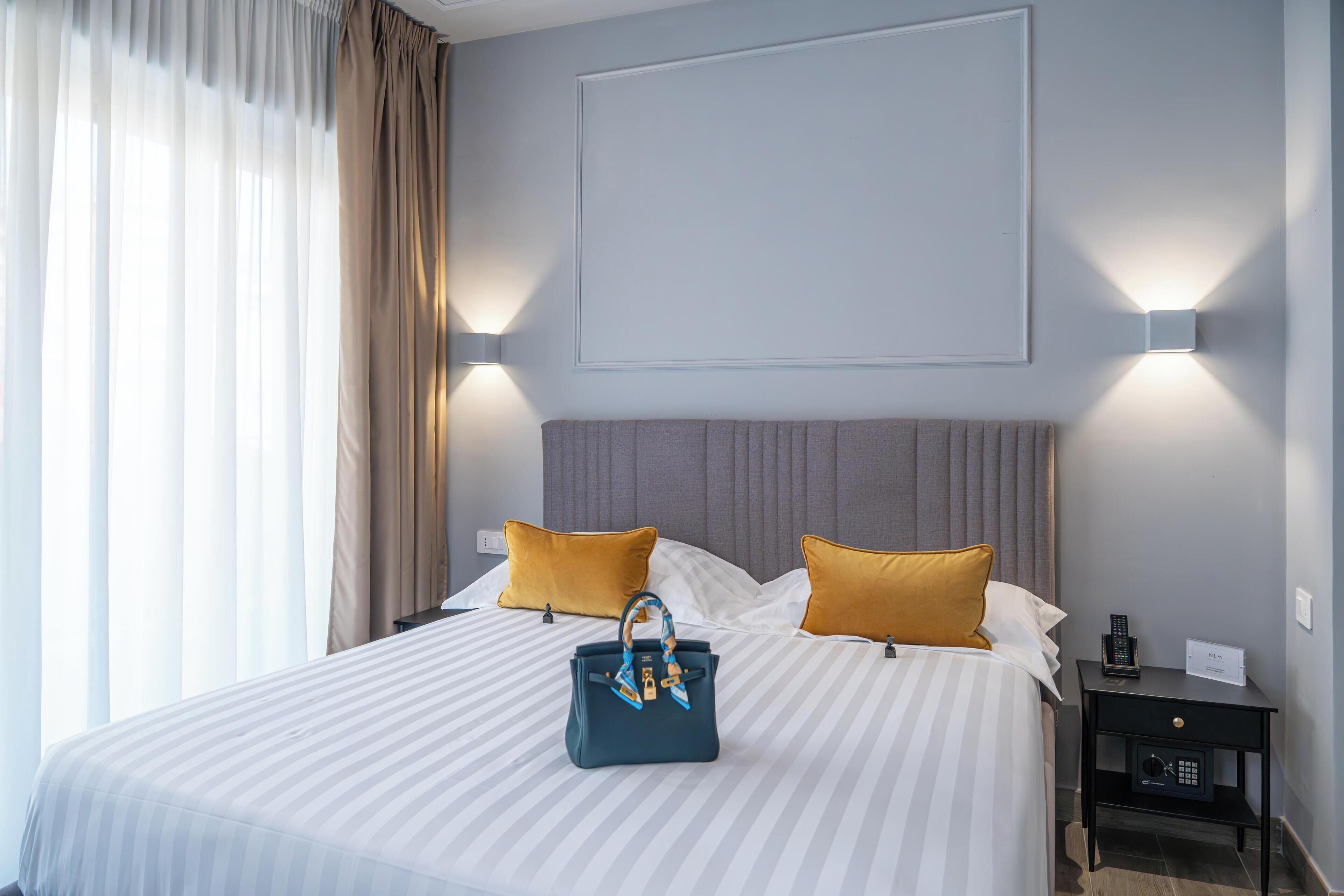 A neatly made bed with striped bedding, two pillows, a bedside table with a lamp, and a handbag on the bed.