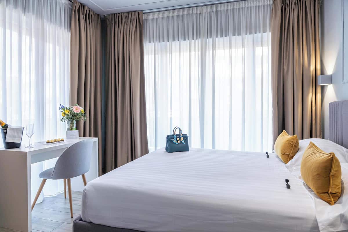 Habitación de hotel con cama, escritorio, silla y ventana con cortinas.