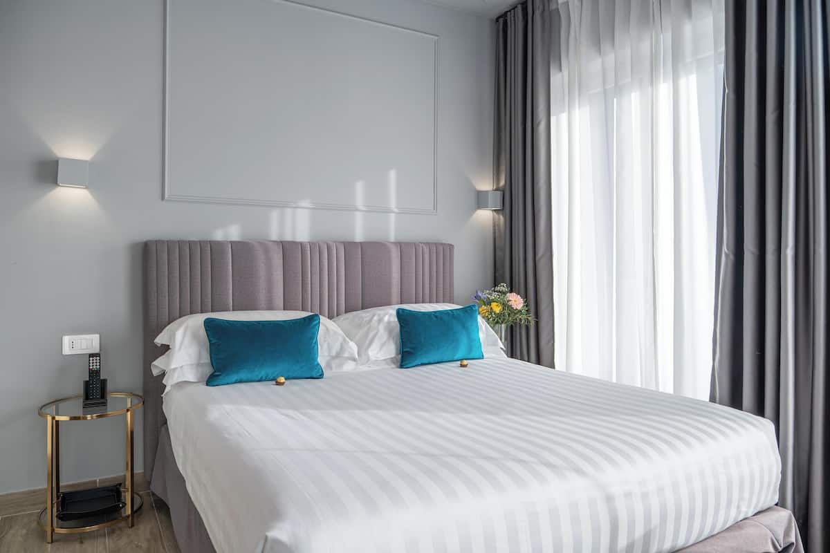 Habitación de hotel con una cama grande, dos almohadas, una mesita de noche con teléfono y una lámpara en la pared.