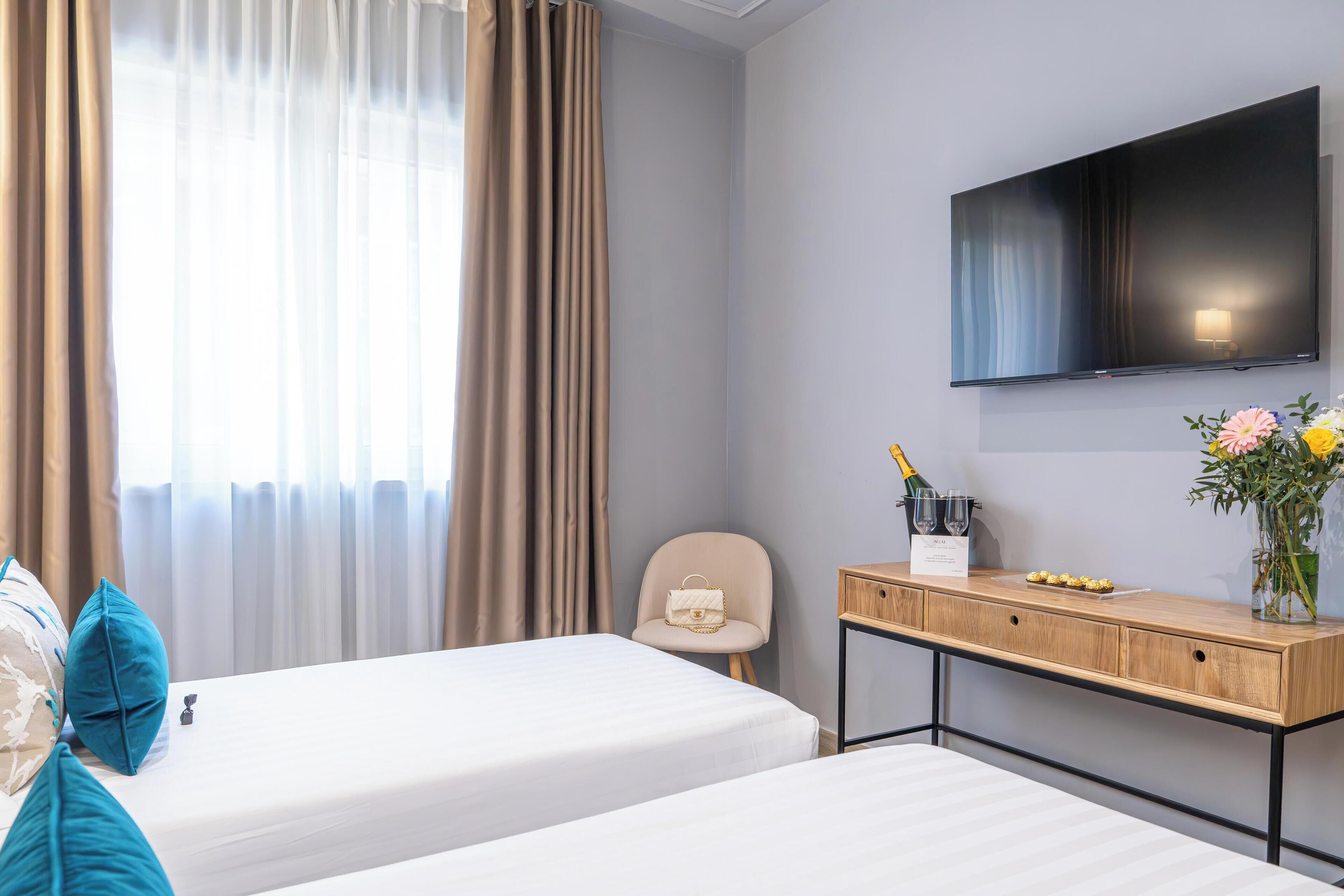 Ein Hotelzimmer mit zwei Betten, einem an der Wand befestigten Fernseher, einem Schreibtisch mit Blumenvase und einem Sessel.