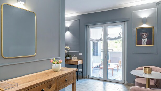 Quarto moderno com escrivaninha de madeira, uma cadeira branca, uma mesa redonda pequena e uma porta de vidro deslizante para área externa.