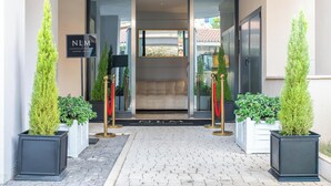 Entrada de um hotel de luxo com design moderno, com porta de vidro, tapete vermelho e plantas em vasos.