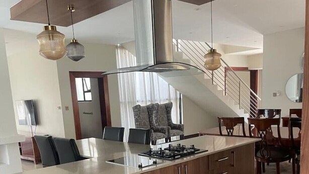 A modern kitchen with a central island, stainless steel range hood, and pendant lighting.