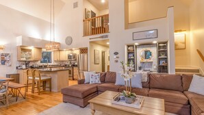 A spacious living area with a brown sectional sofa, a wooden coffee table, and a kitchen with modern appliances. - Relaxing Beach Home Near Dunes & Downtown MC (Michigan City)