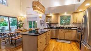 A modern kitchen with wooden cabinets, a stainless steel refrigerator, and a dining area with a table and benches. - Relaxing Beach Home Near Dunes & Downtown MC (Michigan City)