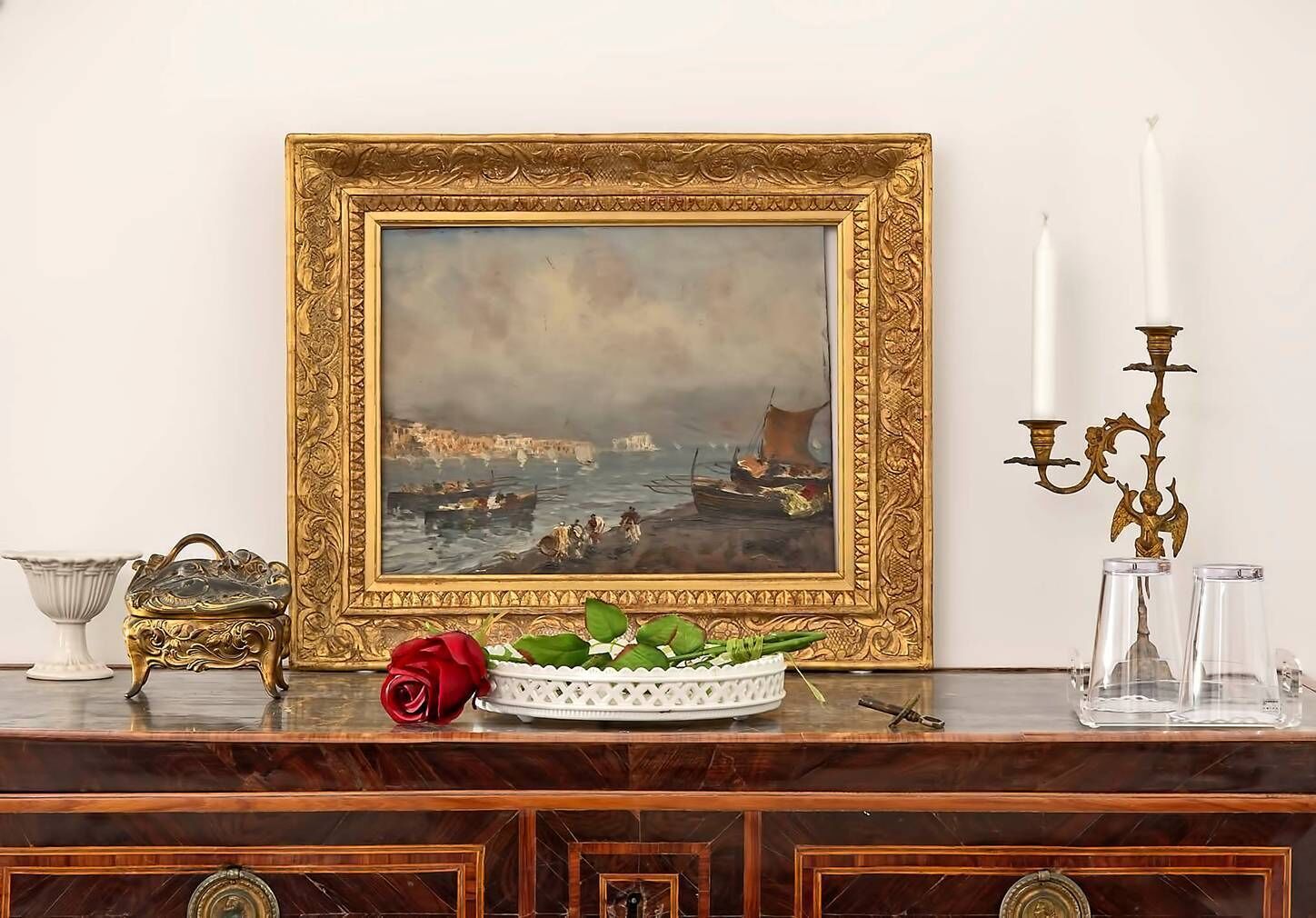 Un cuadro enmarco de un paisaje costero con un candelabro decorativo y un florero sobre una superficie de madera.