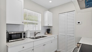 A compact kitchen with a microwave, sink, and white cabinets. - Coral Ridge Suites #1 - Heated Pool, Beach Gear (Fort Lauderdale)