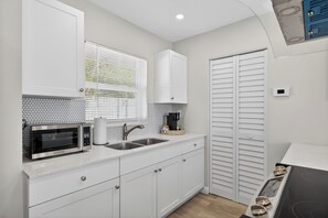 A compact kitchen with a microwave, sink, and white cabinets. - Coral Ridge Suites #1 - Heated Pool, Beach Gear (Fort Lauderdale)