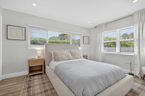 A bedroom with a large bed, two bedside tables, a nightstand, and a window with blinds. - Coral Ridge Suites #1 - Heated Pool, Beach Gear (Fort Lauderdale)