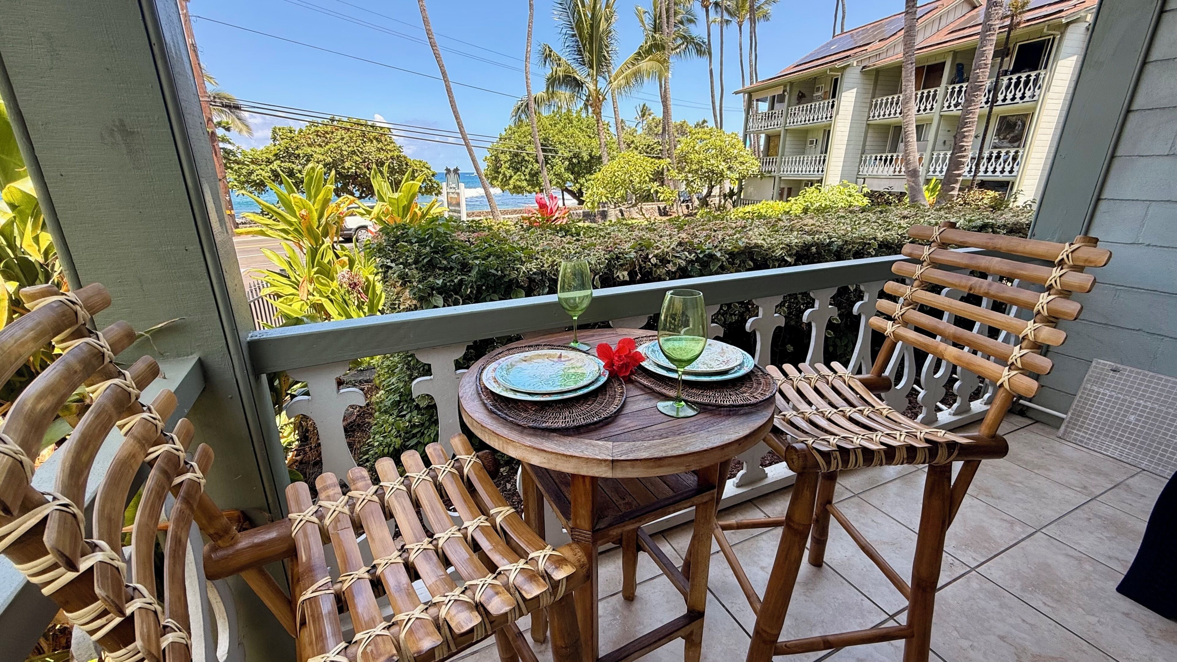 A balcony with a table set for two, two chairs, and a view of a building and palm trees.