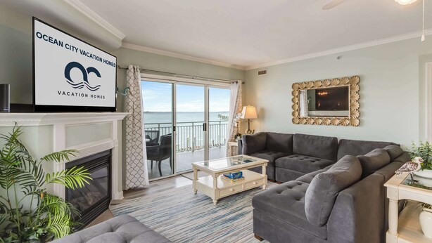 A living room with a fireplace, a sofa, a coffee table, and a view of the ocean through a sliding glass door. - Bahia Vista Unit 201 (Ocean City)