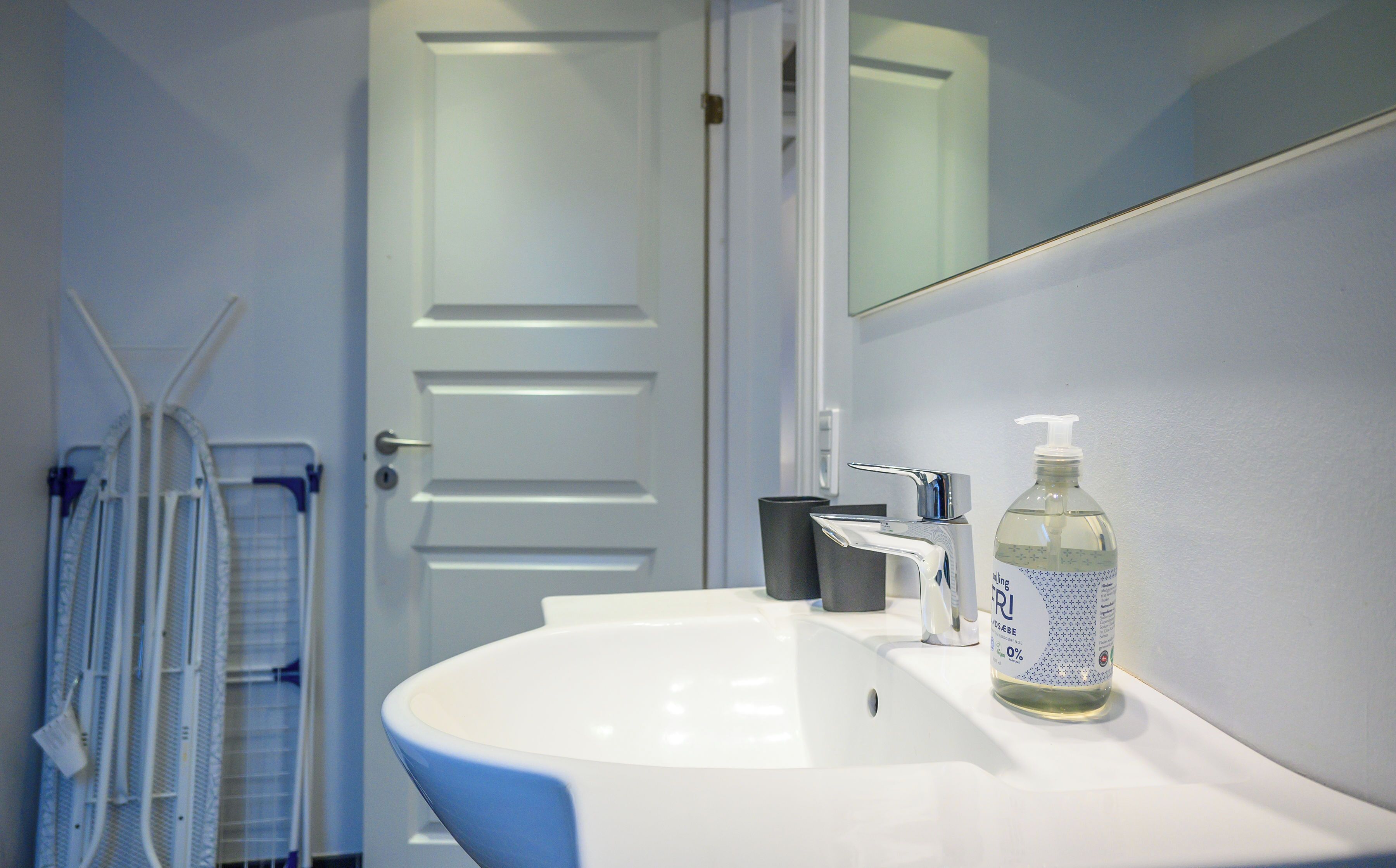 A bathroom with a white sink, a mirror, a door, and a bottle of hand sanitizer.