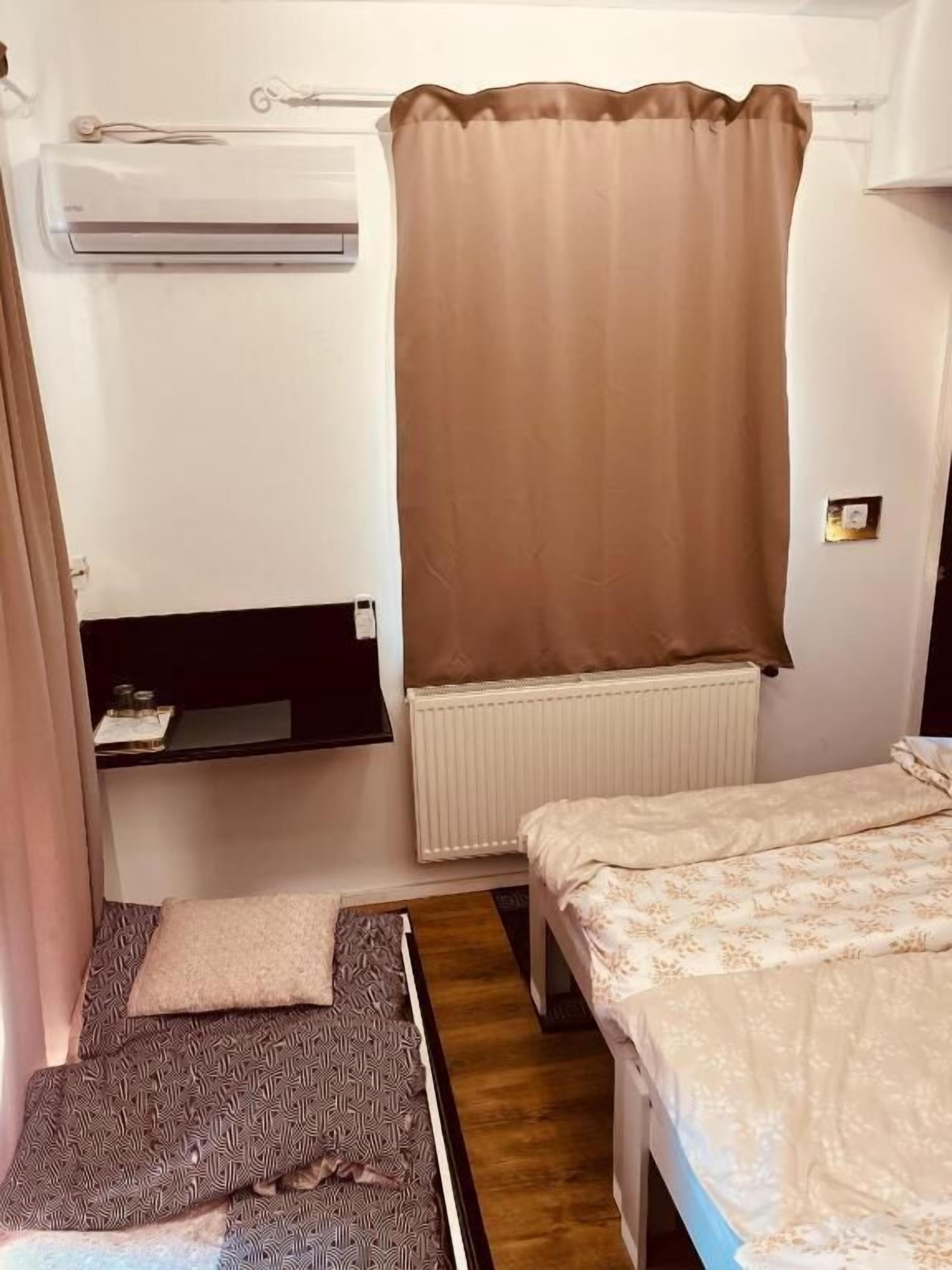 Una habitación pequeña y funcional con una cama individual, una mesita de noche y una ventana con cortina.
