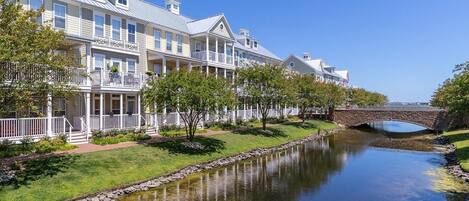 A row of waterfront hotel buildings with balconies, a stone bridge, and a calm water body.