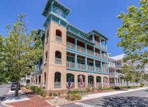 A multi-story building with balconies, a clock tower, and American flags. - Mini Weeks Stays Available Sunset Island 26 Island (Ocean City)