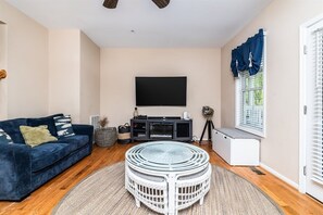 Un salon avec un canapé, un téléviseur, une table basse ronde et une fenêtre avec des rideaux.